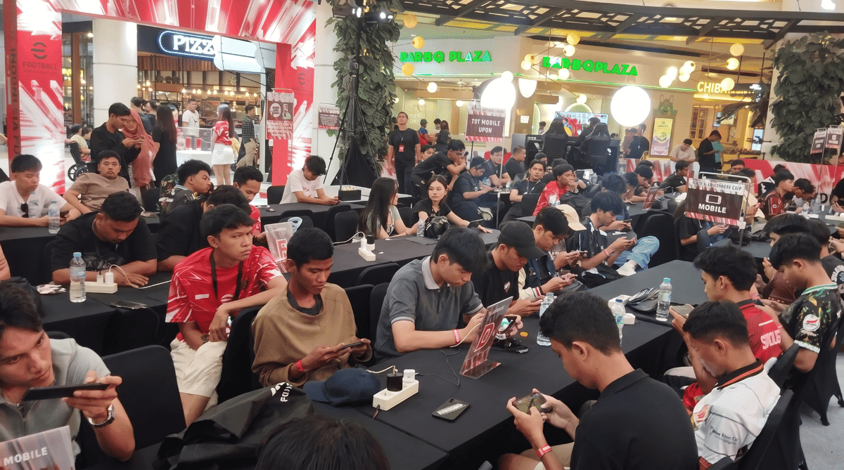 Para peserta eFootball Indonesia Cup 2026 sedang bermain gim di ponsel mereka di area turnamen yang ramai di dalam pusat perbelanjaan.